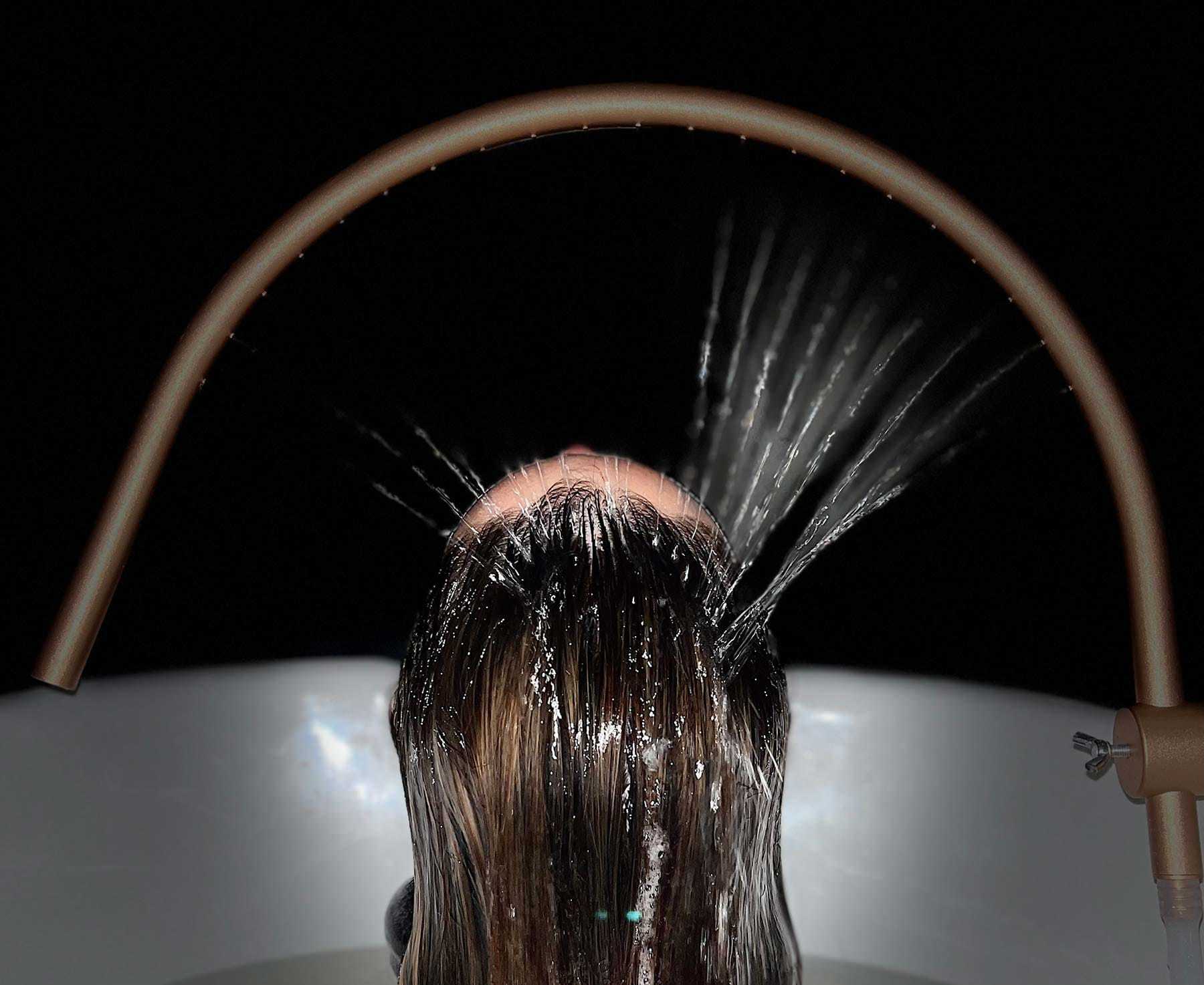 Shower head spraying water on a person's hair in a dark setting.