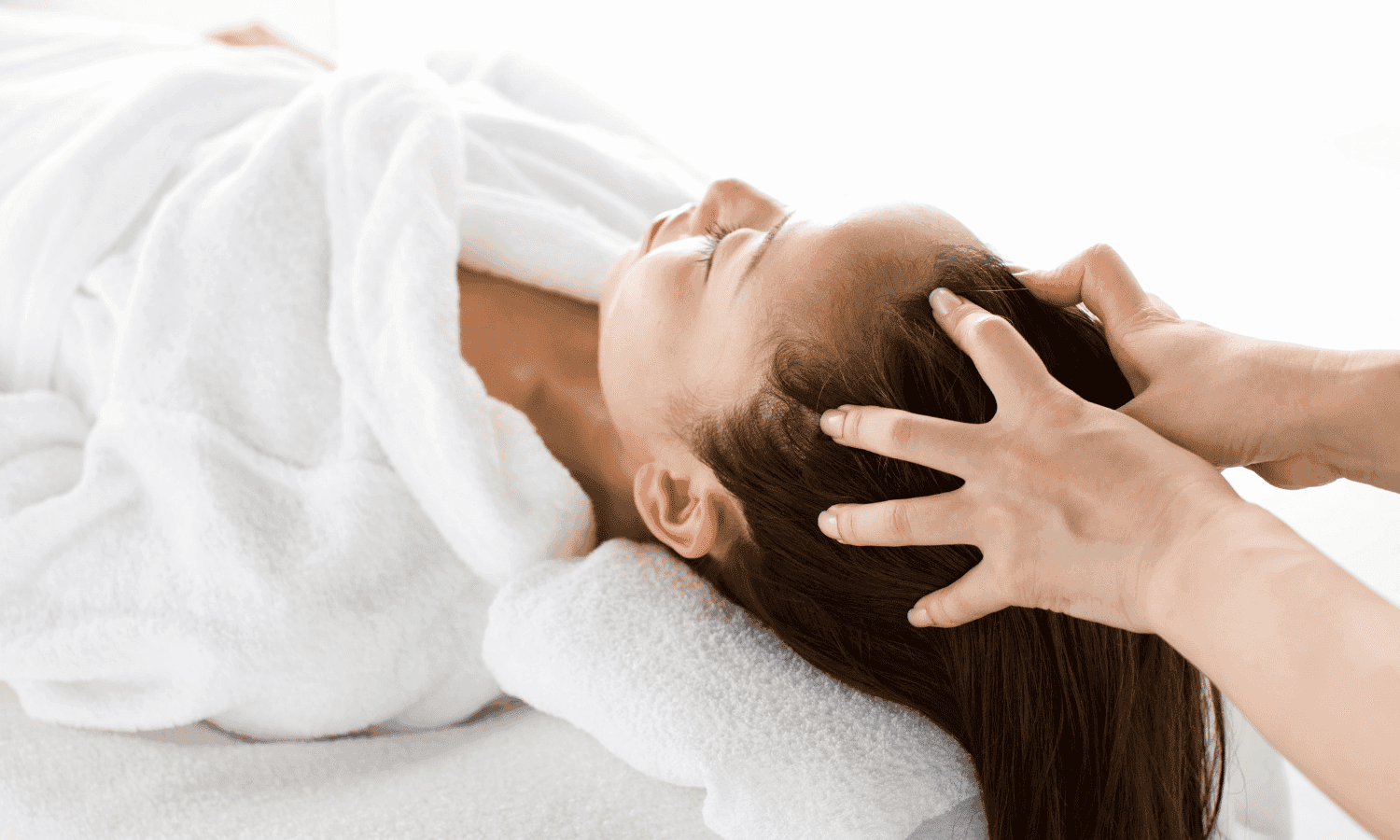 Head massage in spa, person lying relaxed on towel, hands applying gentle pressure on scalp.