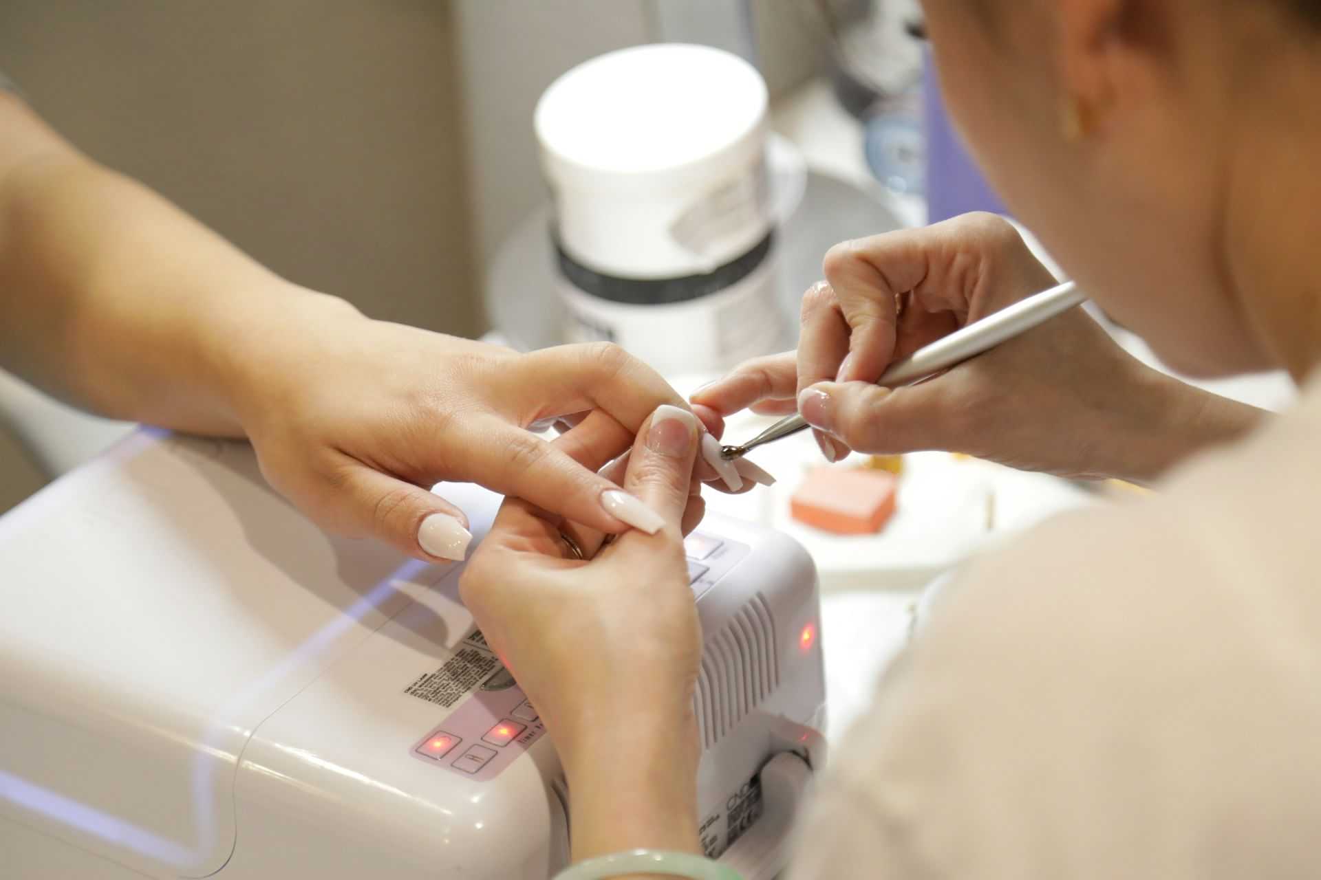 Nail technician manicuring a client's nails with precision tools in a salon.